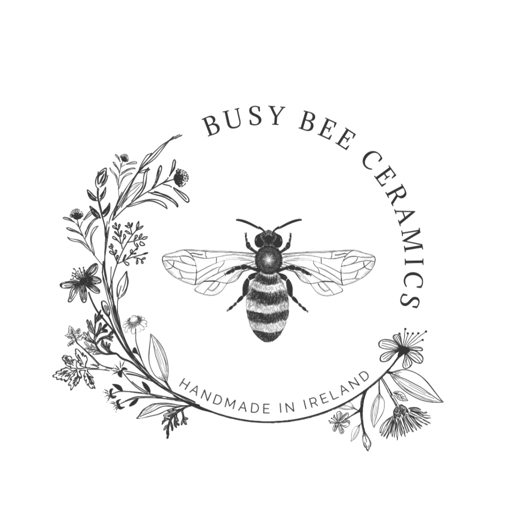 The Busy Bee Ceramics emblem over a soft-focus Irish countryside at dawn.