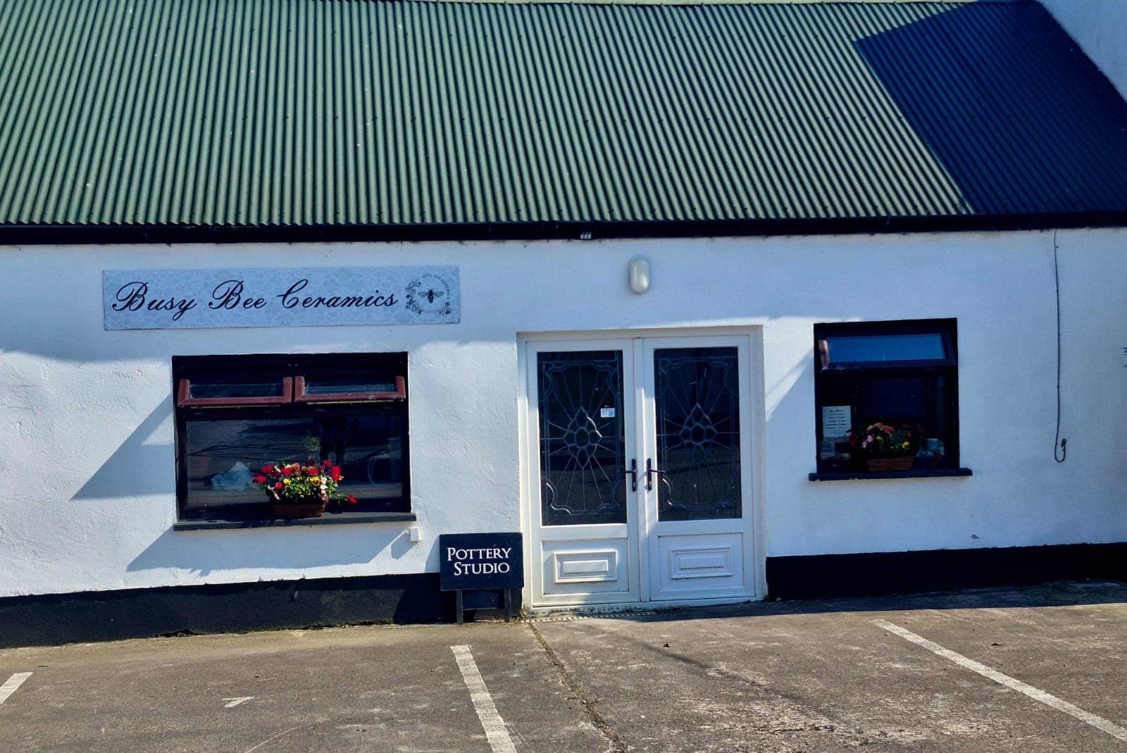 The whitewashed front of the Busy Bee Ceramics studio, with its green corrugated roof and hand-painted sign